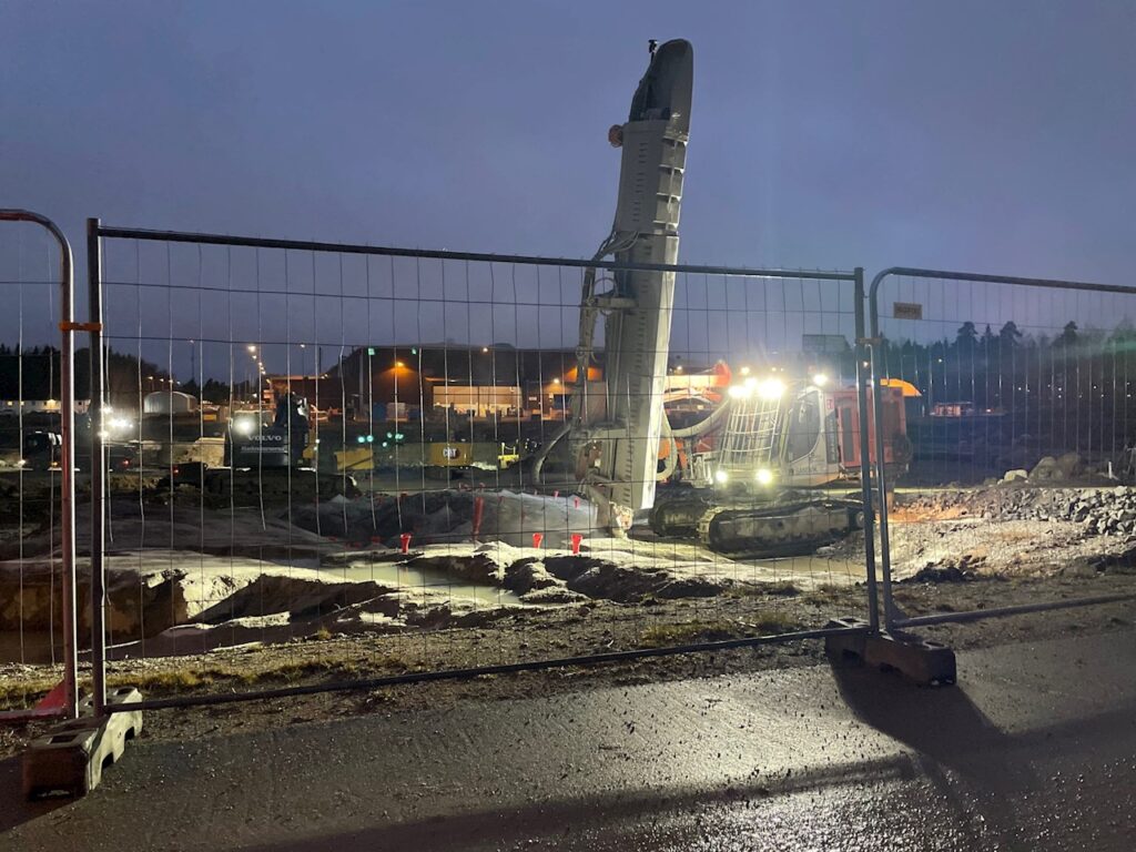 Borrigg arbetar på en upplyst byggarbetsplats vid Robotics Campus i Västerås under kvällstid, bakom ett avspärrningsstängsel.
